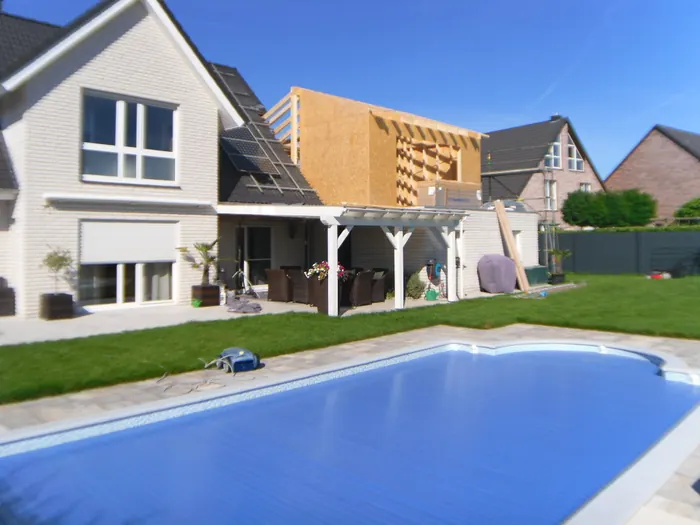 Wohnhaus mit neuem Holzaufbau über dem Erdgeschossdach, davor eine Pergola am Poolbereich