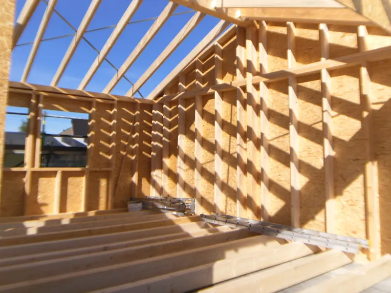 Blick in einen neuen Dachstuhl: Sparren und Holzständerwände im Sonnenlicht