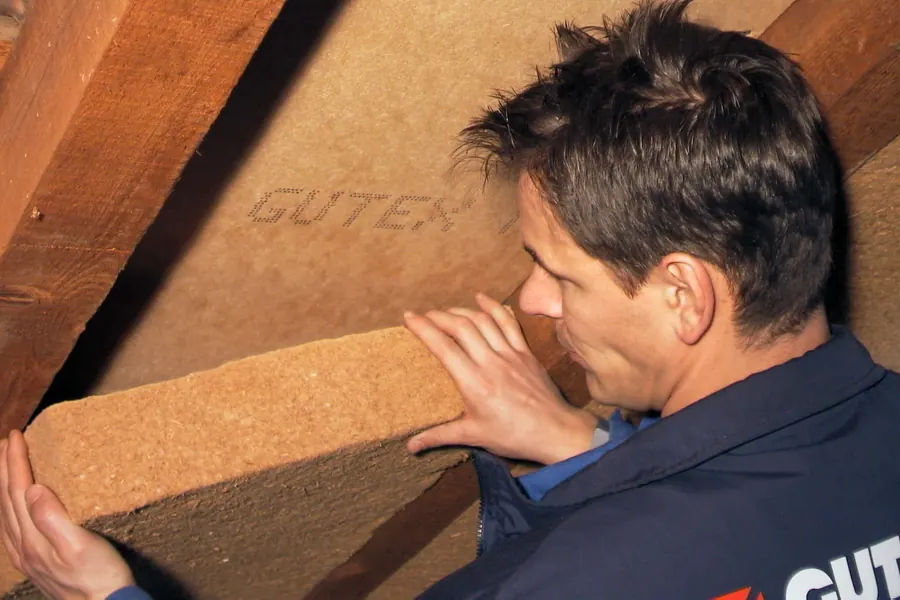 Handwerker setzt eine Holzfaser-Dämmplatte zwischen die Dachsparren