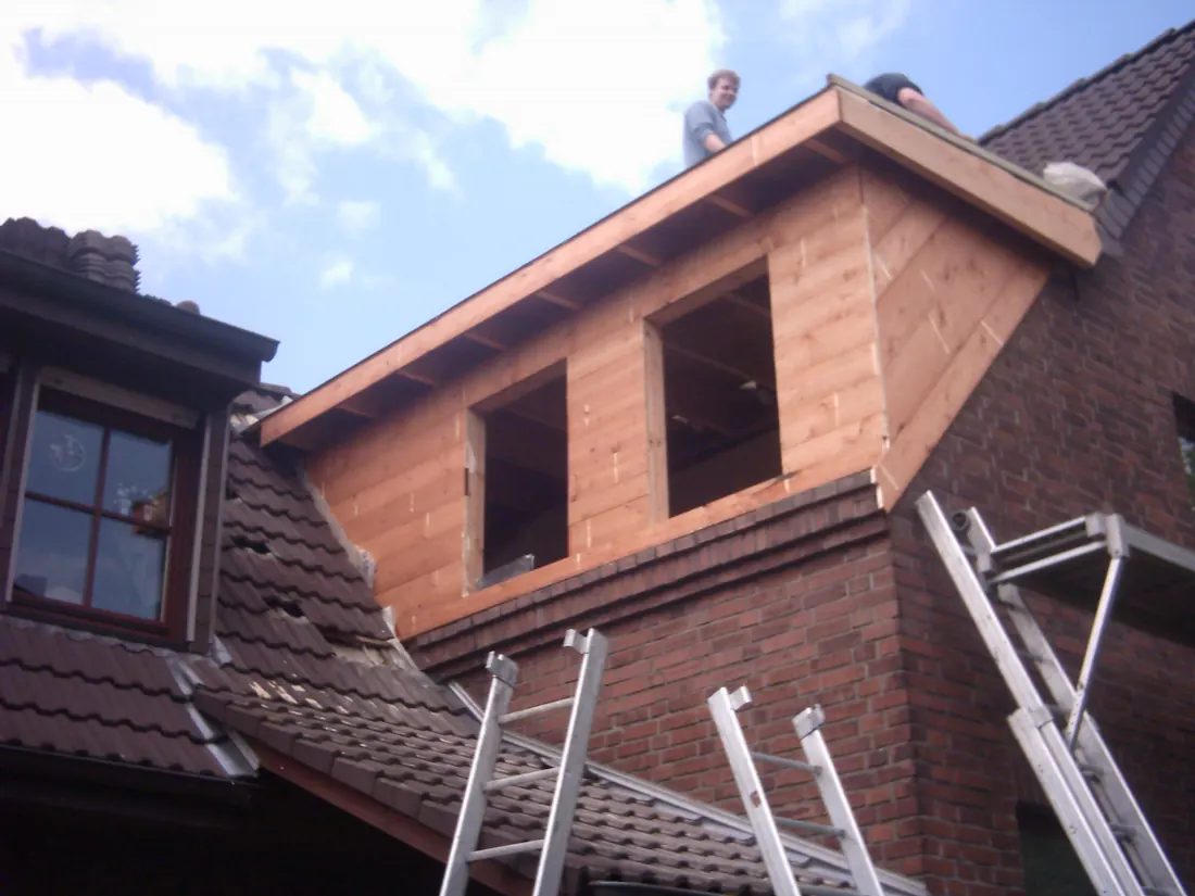 Neu aufgebaute Dachgaube aus Holz auf einem Ziegeldach, Leitern am Haus