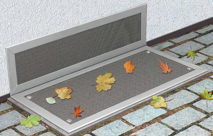 Aufgeklappte Lichtschacht-Abdeckung mit Insektenschutzgitter im Aluminiumrahmen, darauf Herbstlaub