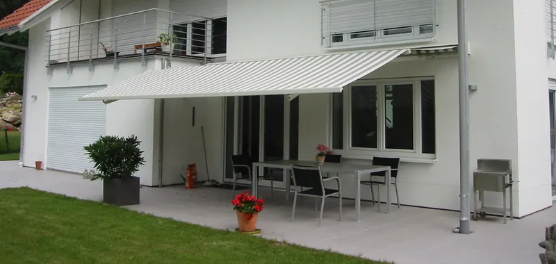 Markise an einer hellen Hausfassade, ausgefahren über der Terrasse mit Esstisch