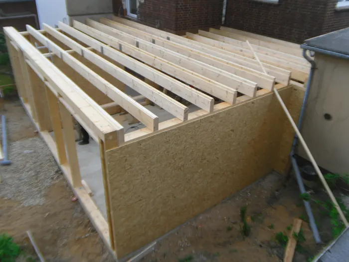 Tragende Holz-Unterkonstruktion mit Balkenlage auf der Baustelle vor einem Backsteinhaus