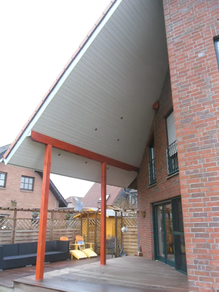 Überdachung mit weiß verschalter Untersicht und roten Holzstützen über einer Terrasse an einem Backsteinhaus