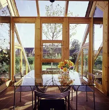 Blick von innen in einen Wintergarten aus Holz mit Esstisch und geöffneten Fensterflügeln