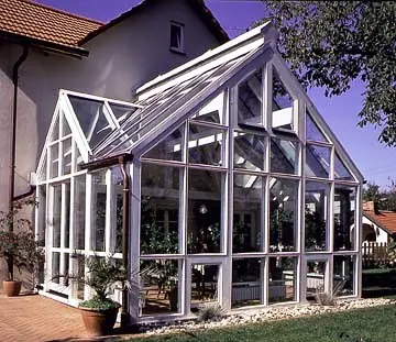 Wintergarten mit weißem Rahmenwerk und Satteldach an einem verputzten Wohnhaus