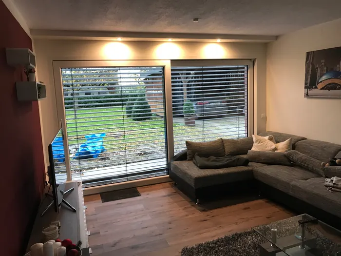 Wohnraum mit großem Fensterelement, Raffstore und Blick in den Garten